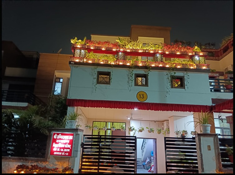 The finished facade at night, rooftop planters lit up, Hindi nameplate visible